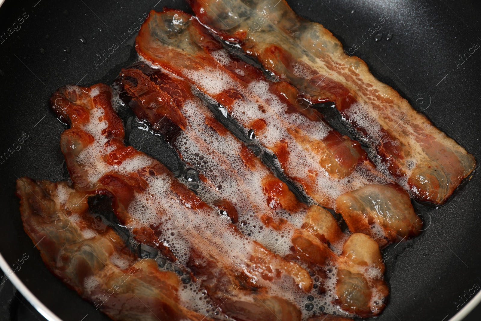 Photo of Slices of bacon frying in pan, closeup