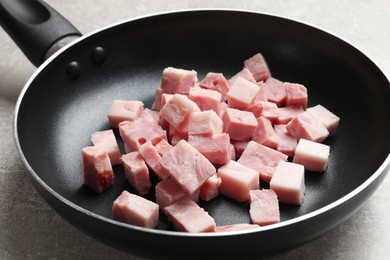 Photo of Pieces of fresh bacon in frying pan on grey textured table, closeup