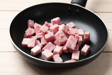 Pieces of fresh bacon in frying pan on light wooden table, closeup