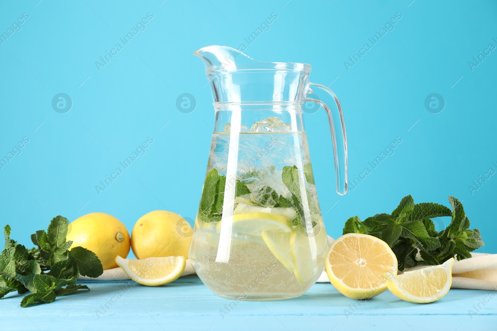 Photo of Refreshing lemonade with mint in jug and ingredients on light blue wooden table