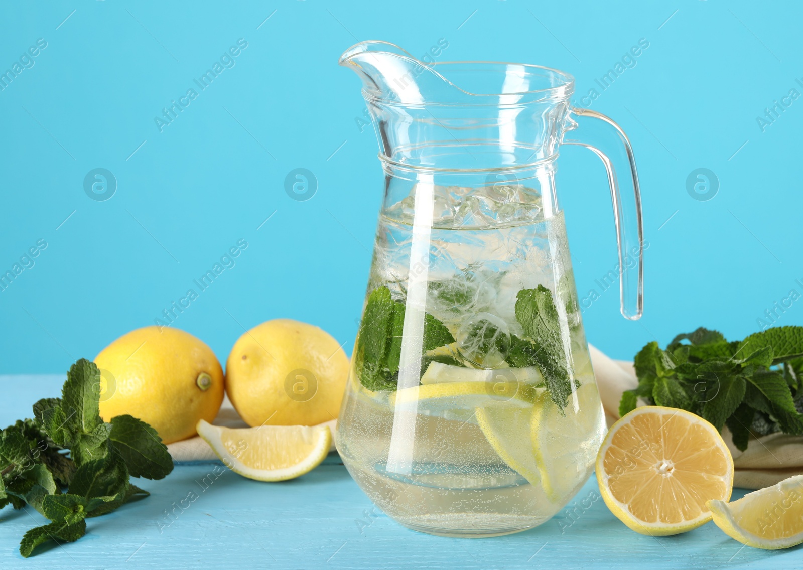 Photo of Refreshing lemonade with mint in jug and ingredients on light blue wooden table