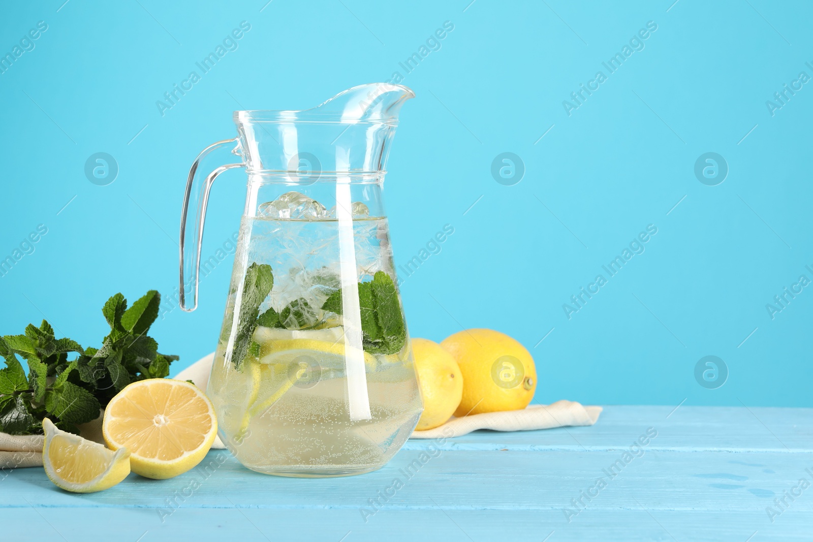 Photo of Refreshing lemonade with mint in jug and ingredients on light blue wooden table, space for text