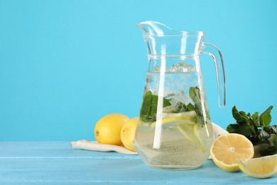 Refreshing lemonade with mint in jug and ingredients on light blue wooden table, space for text