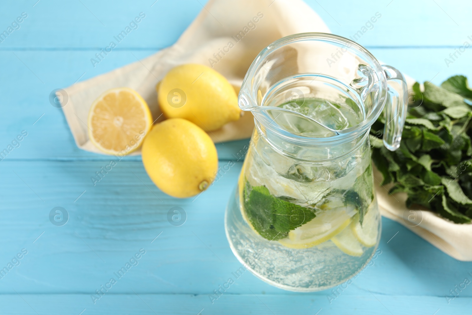 Photo of Refreshing lemonade with mint in jug and ingredients on light blue wooden table