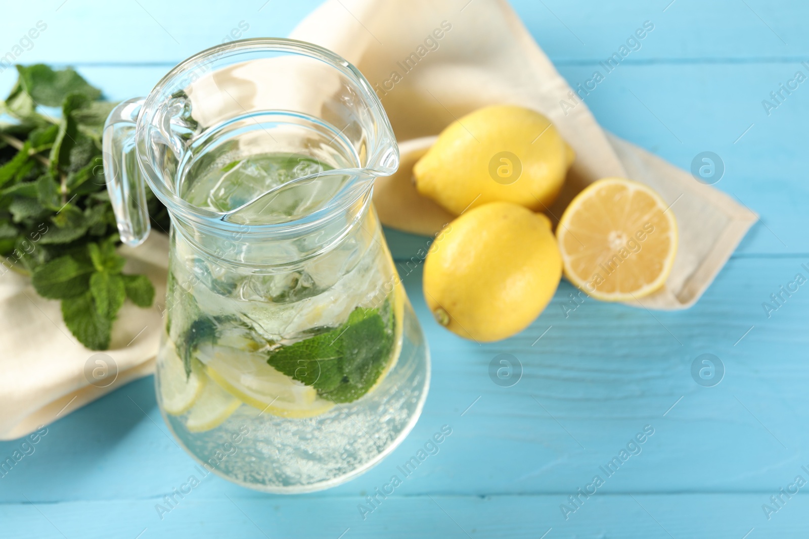 Photo of Refreshing lemonade with mint in jug and ingredients on light blue wooden table