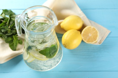 Photo of Refreshing lemonade with mint in jug and ingredients on light blue wooden table