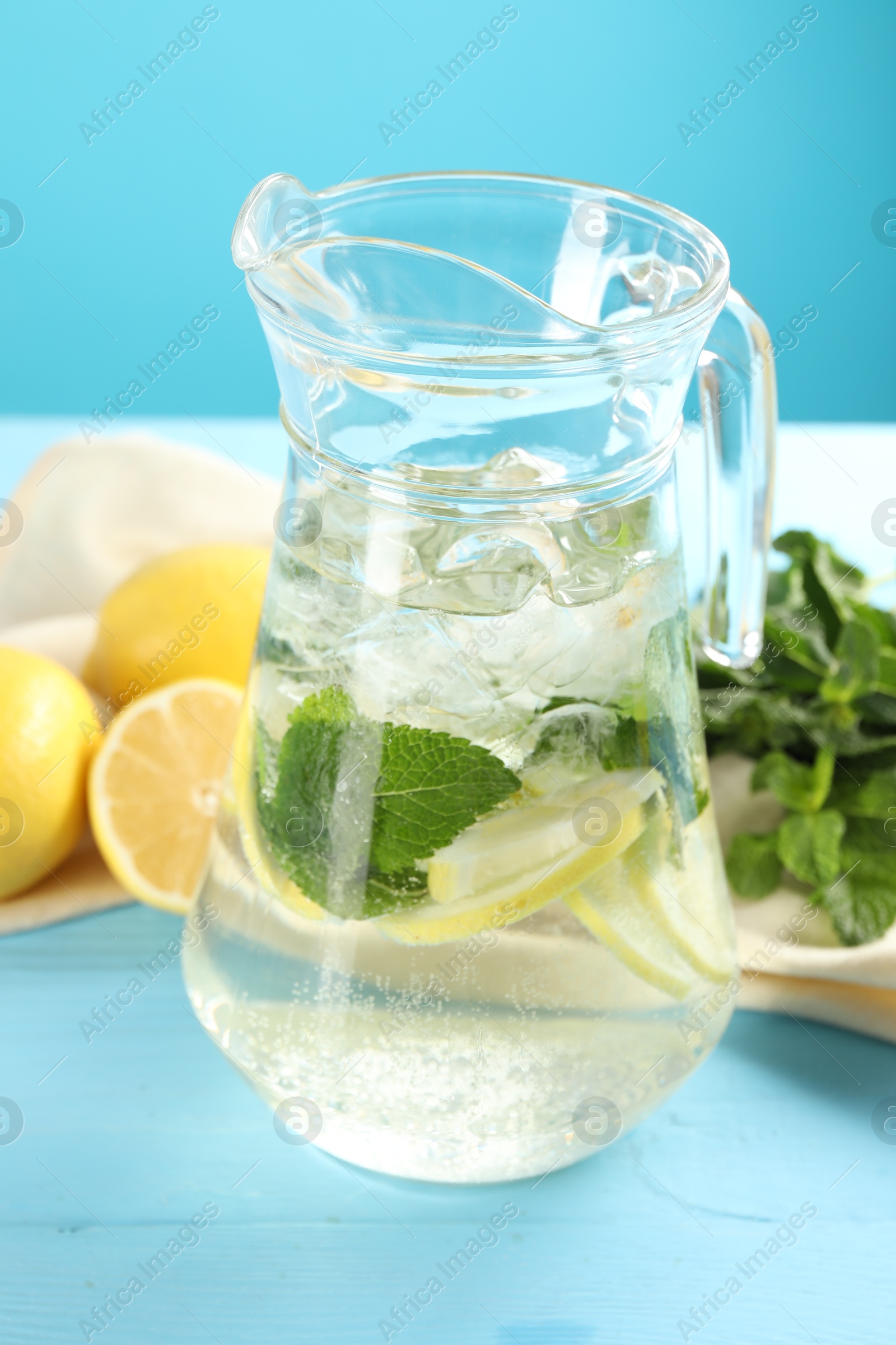 Photo of Refreshing lemonade with mint in jug on light blue wooden table