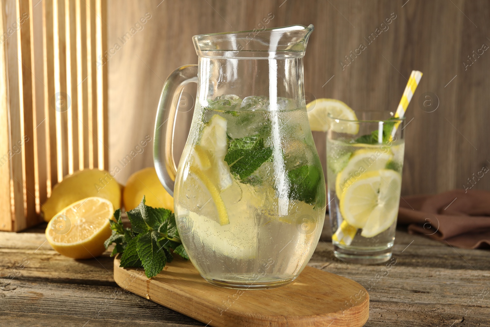 Photo of Refreshing lemonade with mint in jug and glass on wooden table