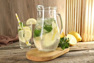 Photo of Refreshing lemonade with mint in jug and glass on wooden table