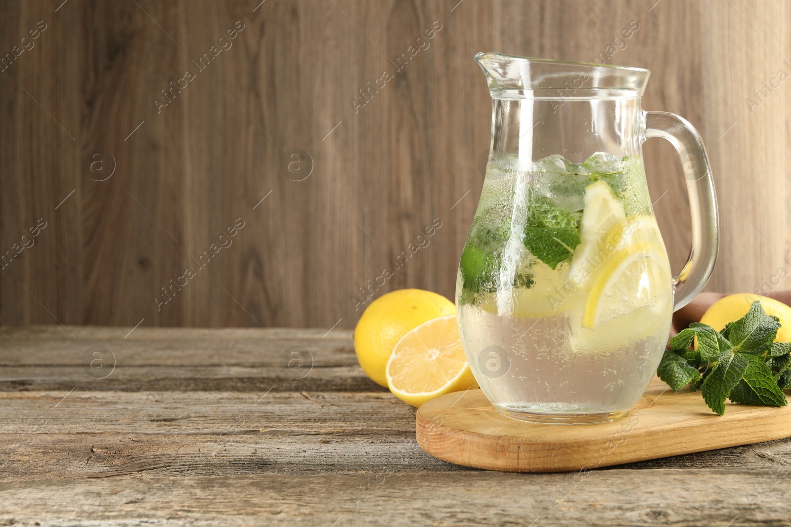 Photo of Refreshing lemonade with mint in jug and ingredients on wooden table, space for text