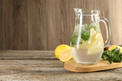 Refreshing lemonade with mint in jug and ingredients on wooden table, space for text