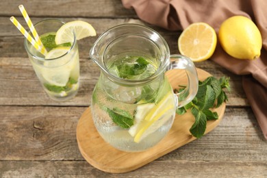 Refreshing lemonade with mint in jug and glass on wooden table