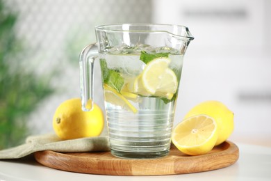 Refreshing lemonade with mint in jug and citrus fruits on white table