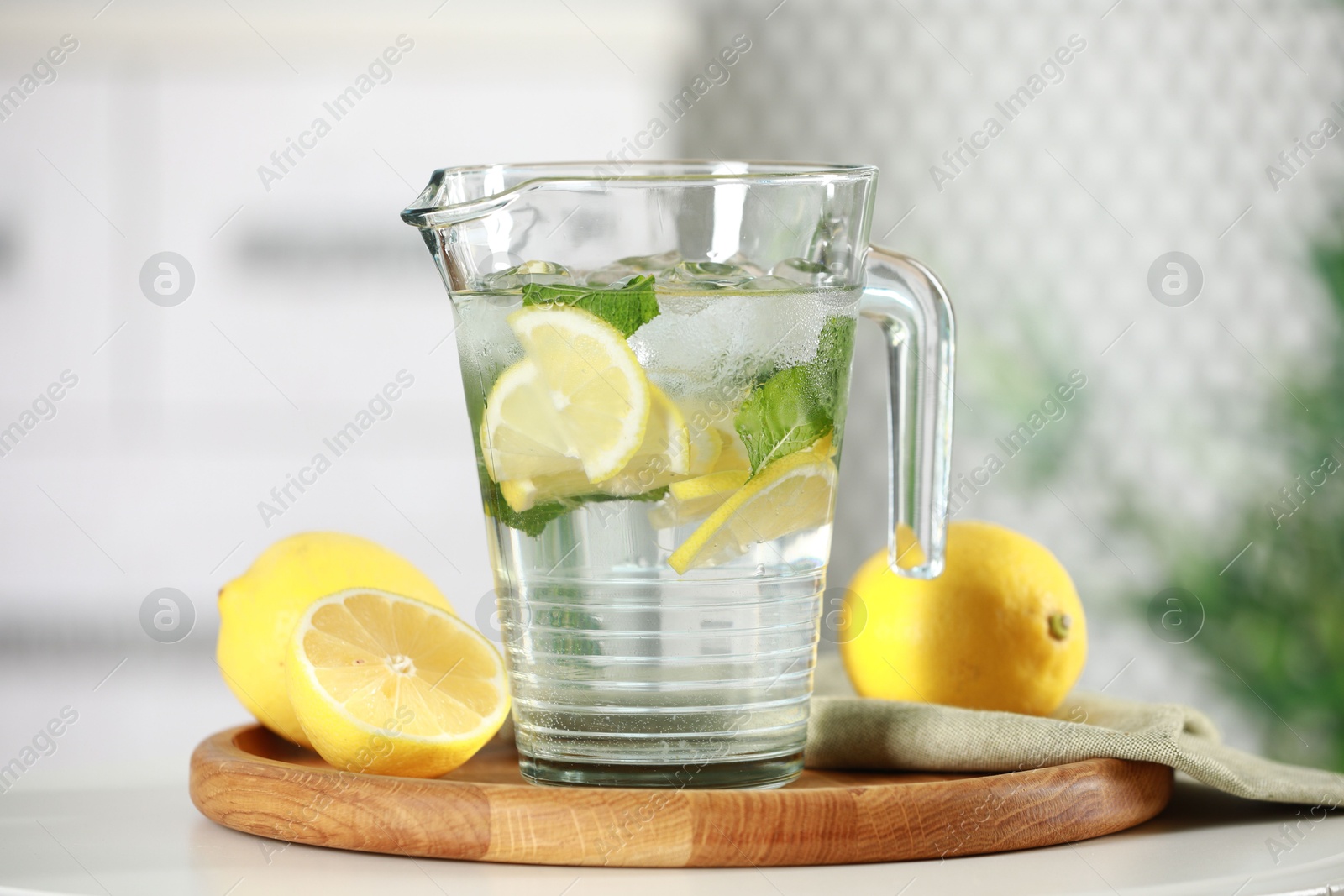 Photo of Refreshing lemonade with mint in jug and citrus fruits on white table