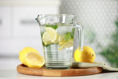 Photo of Refreshing lemonade with mint in jug and citrus fruits on white table