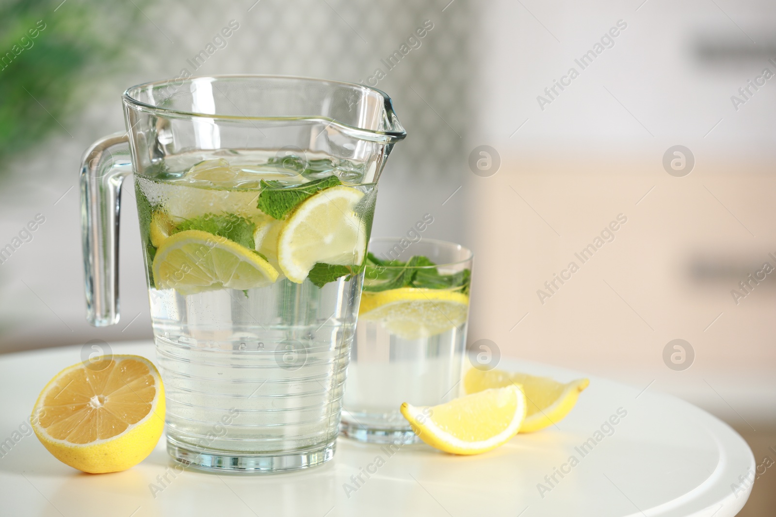 Photo of Refreshing lemonade with mint in jug and glass on white table. Space for text