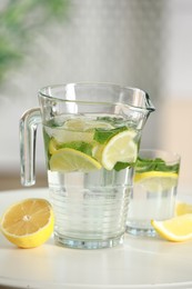 Refreshing lemonade with mint in jug and glass on white table