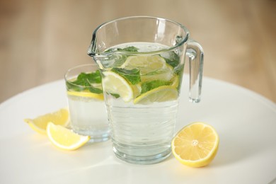 Refreshing lemonade with mint in jug and glass on white table