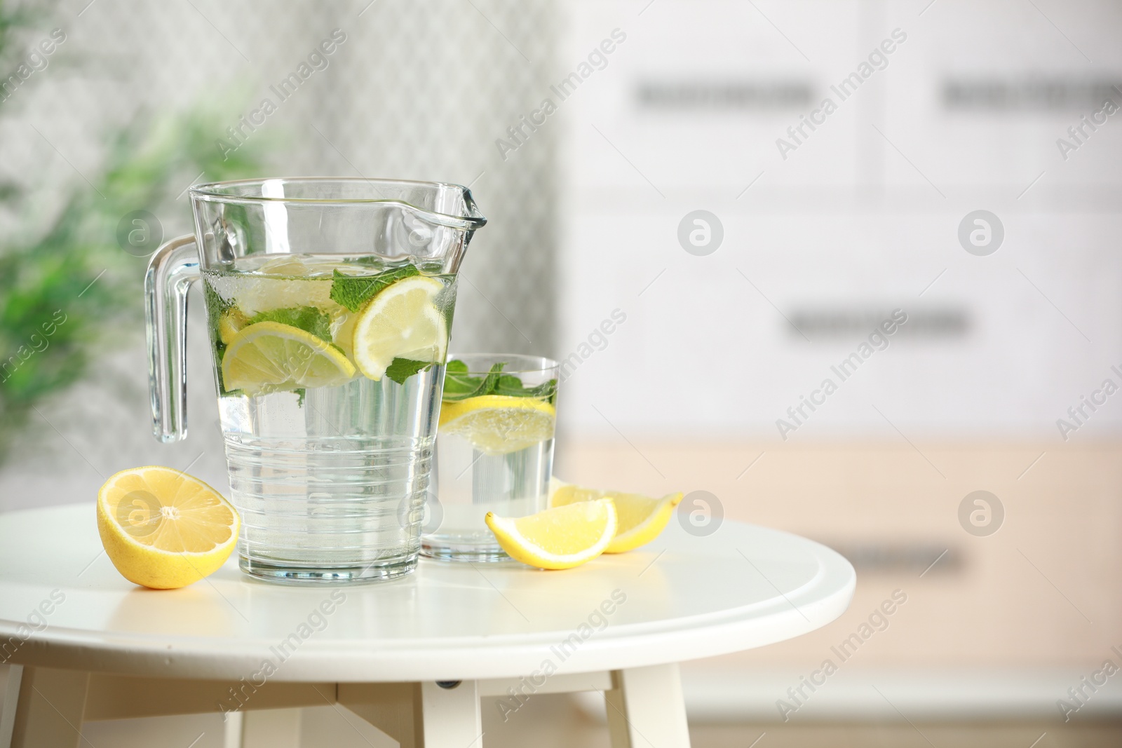 Photo of Refreshing lemonade with mint in jug and glass on white table. Space for text