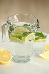 Refreshing lemonade with mint in jug and glass on white table