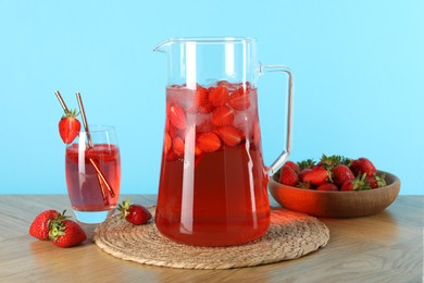 Tasty strawberry lemonade in jug, glass and berries on wooden table against light blue background