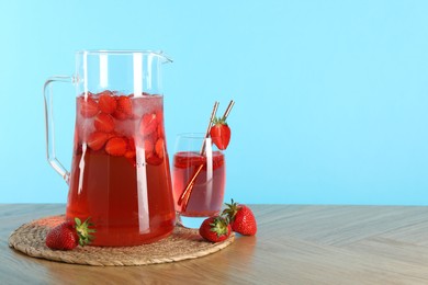 Photo of Tasty strawberry lemonade in jug, glass and berries on wooden table against light blue background. Space for text