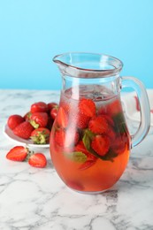 Tasty strawberry lemonade with mint in jug and berries on white marble table against light blue background