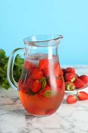 Tasty strawberry lemonade with mint in jug and berries on white marble table against light blue background