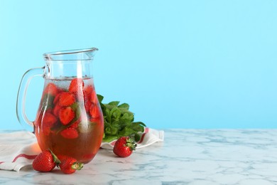 Photo of Tasty strawberry lemonade with mint in jug and berries on white marble table against light blue background. Space for text