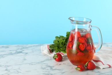 Photo of Tasty strawberry lemonade with mint in jug and berries on white marble table against light blue background. Space for text