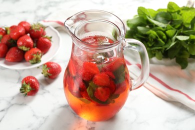 Tasty strawberry lemonade with mint in jug and berries on white marble table, closeup