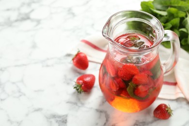 Photo of Tasty strawberry lemonade with mint in jug and berries on white marble table, closeup. Space for text