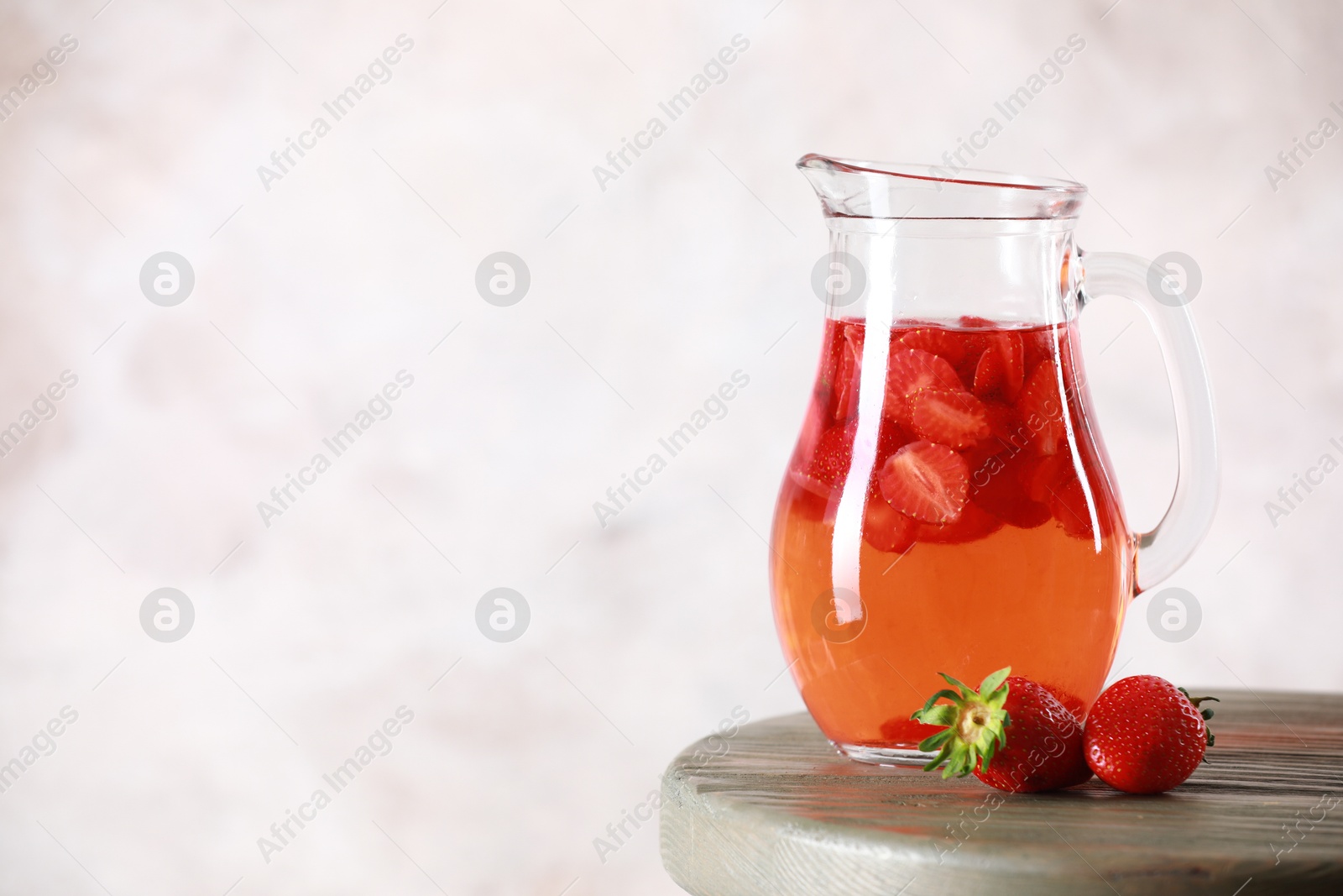 Photo of Tasty strawberry lemonade in jug and berries on wooden table against light background. Space for text