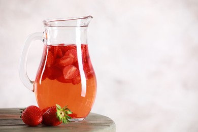 Photo of Tasty strawberry lemonade in jug and berries on wooden table against light background, closeup. Space for text