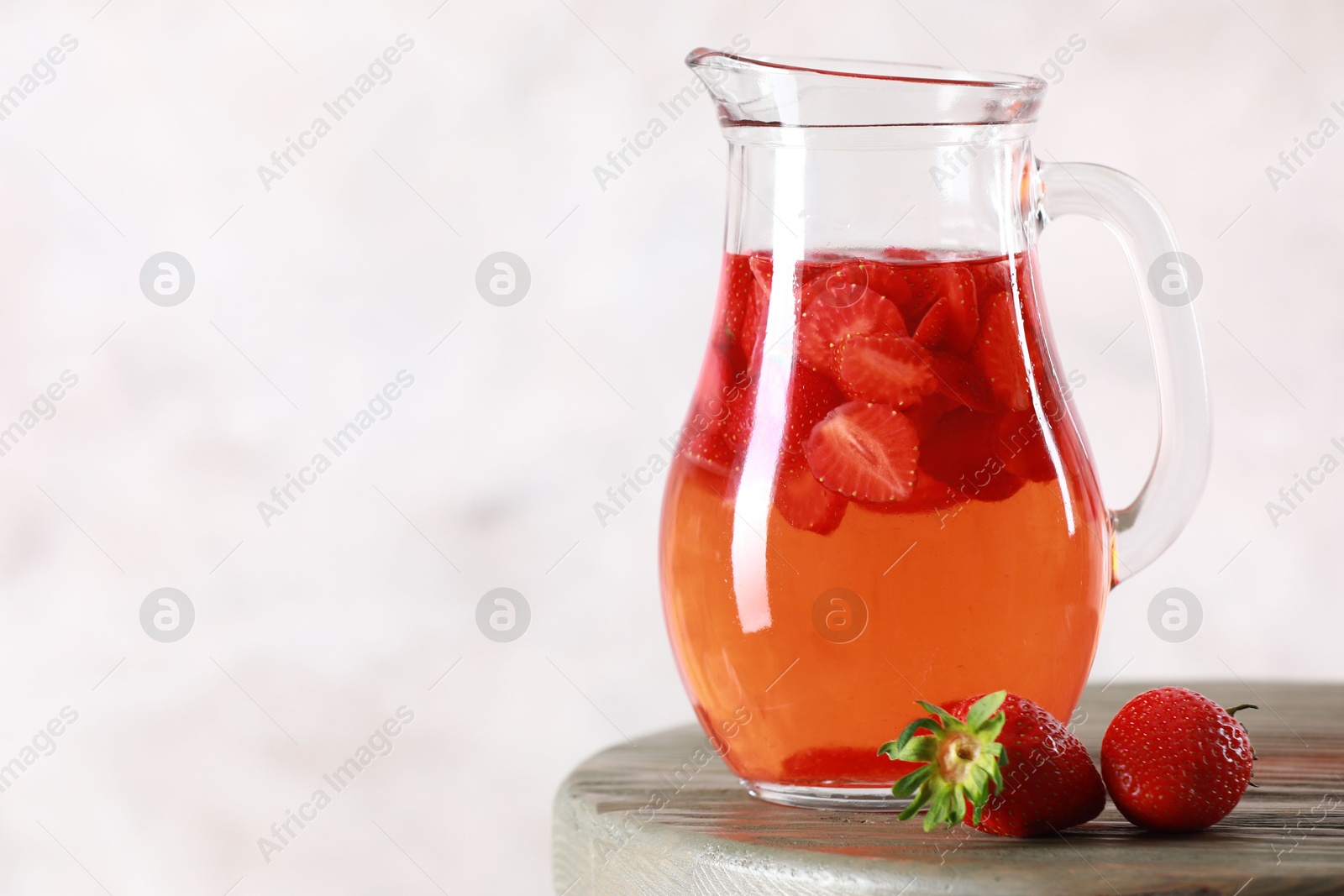 Photo of Tasty strawberry lemonade in jug and berries on wooden table against light background, closeup. Space for text