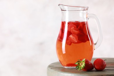 Photo of Tasty strawberry lemonade in jug and berries on wooden table against light background, closeup. Space for text