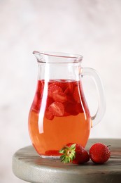 Tasty strawberry lemonade in jug and berries on wooden table against light background