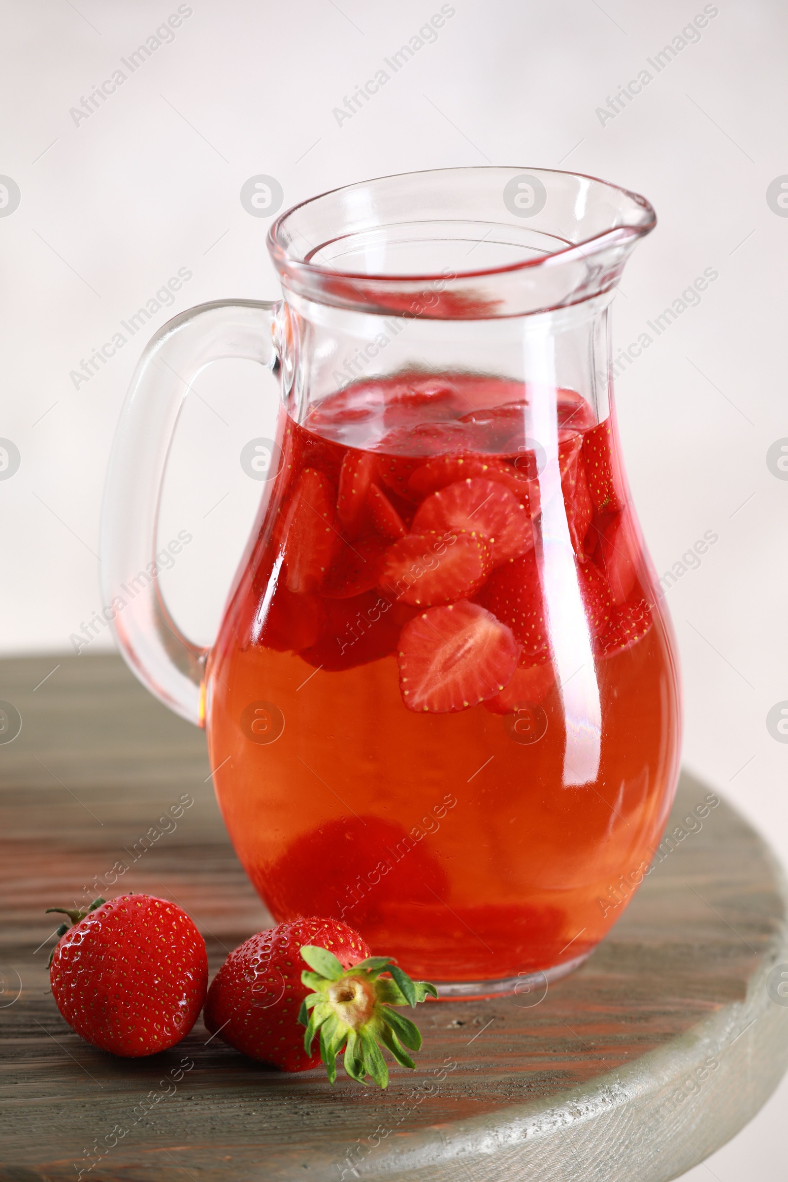 Photo of Tasty strawberry lemonade in jug and berries on wooden table against light background