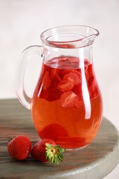 Tasty strawberry lemonade in jug and berries on wooden table against light background