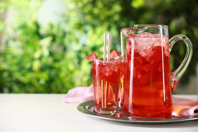 Tasty strawberry lemonade in jug and glasses on white table against blurred green background. Space for text