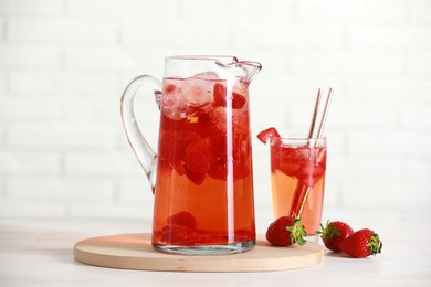 Photo of Tasty strawberry lemonade in jug, glass and berries on white wooden table