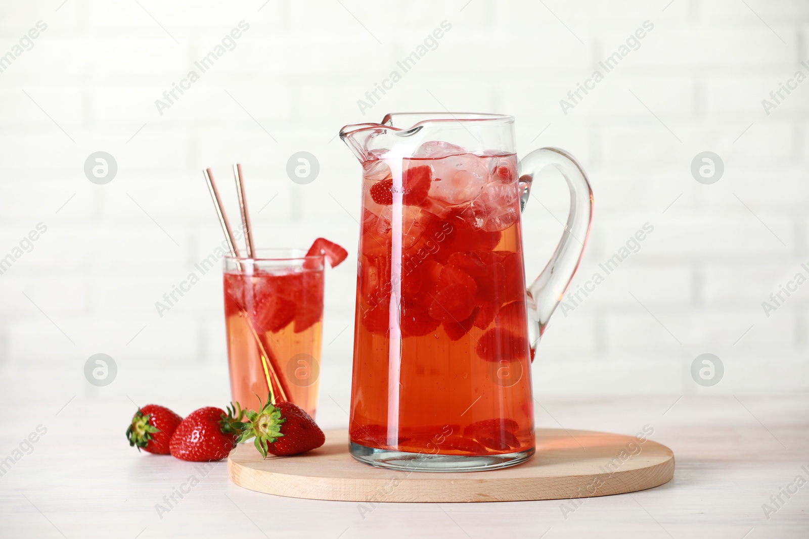 Photo of Tasty strawberry lemonade in jug, glass and berries on white wooden table