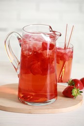 Photo of Tasty strawberry lemonade in jug, glass and berries on white wooden table