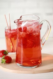 Photo of Tasty strawberry lemonade in jug, glass and berries on white wooden table