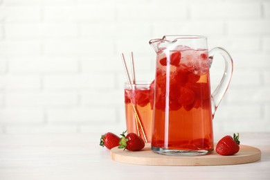 Photo of Tasty strawberry lemonade in jug, glass and berries on white wooden table, space for text