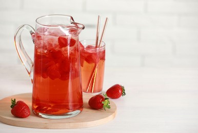 Tasty strawberry lemonade in jug, glass and berries on white wooden table, space for text