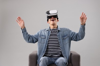 Photo of Emotional young man with virtual reality headset sitting on armchair against light grey background