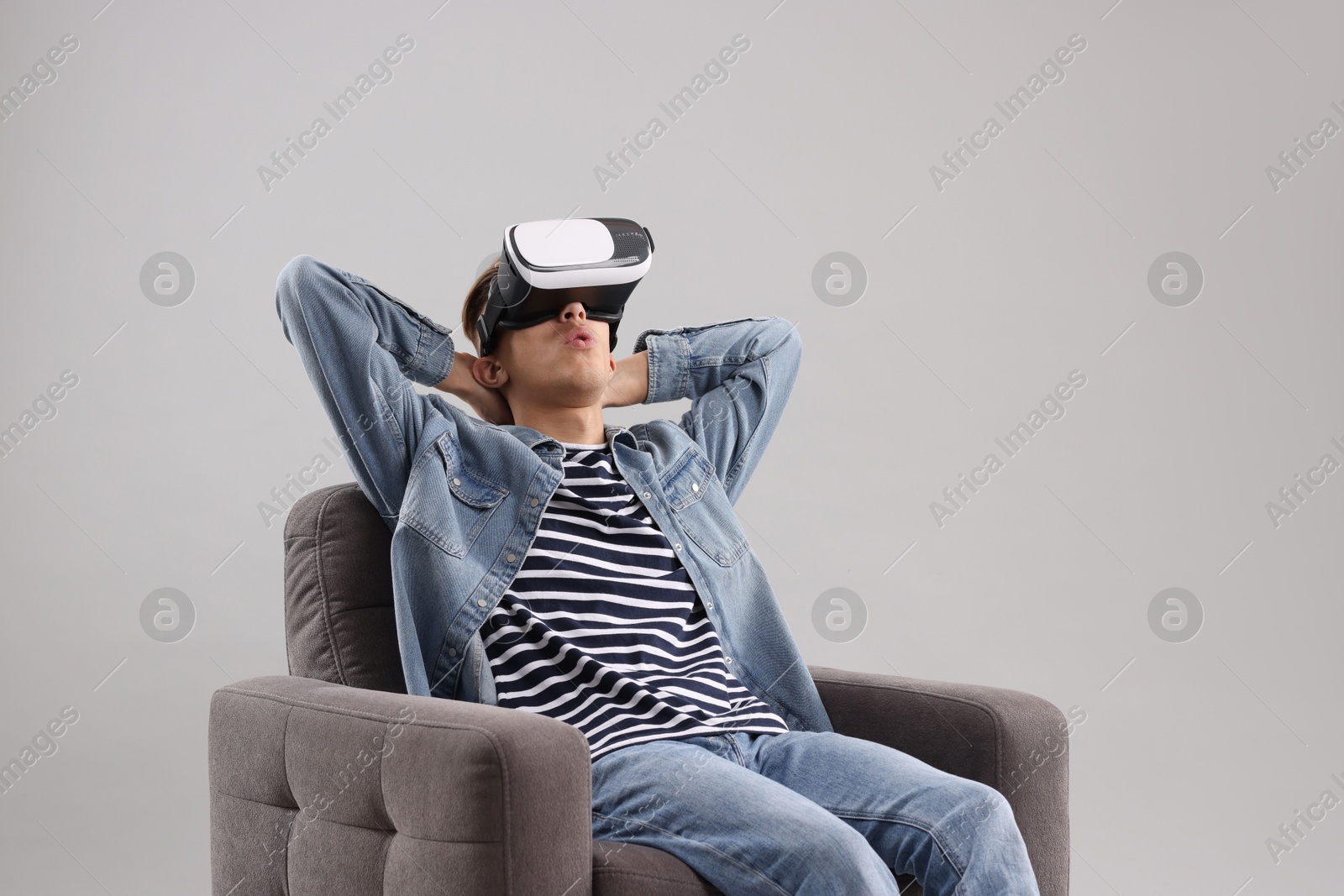 Photo of Emotional young man with virtual reality headset sitting on armchair against light grey background, space for text