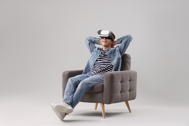 Photo of Happy young man with virtual reality headset sitting on armchair against light grey background