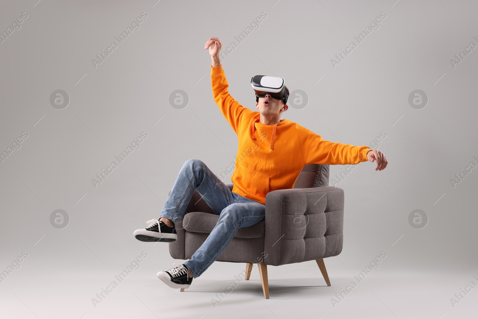 Photo of Emotional young man with virtual reality headset sitting on armchair against light grey background